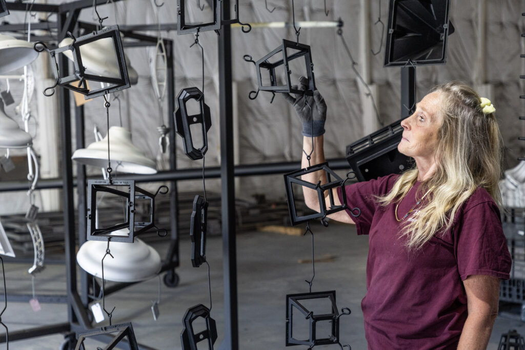 A lady in a maroon shirt is checking her work. She has lighting frames hanging to dry.