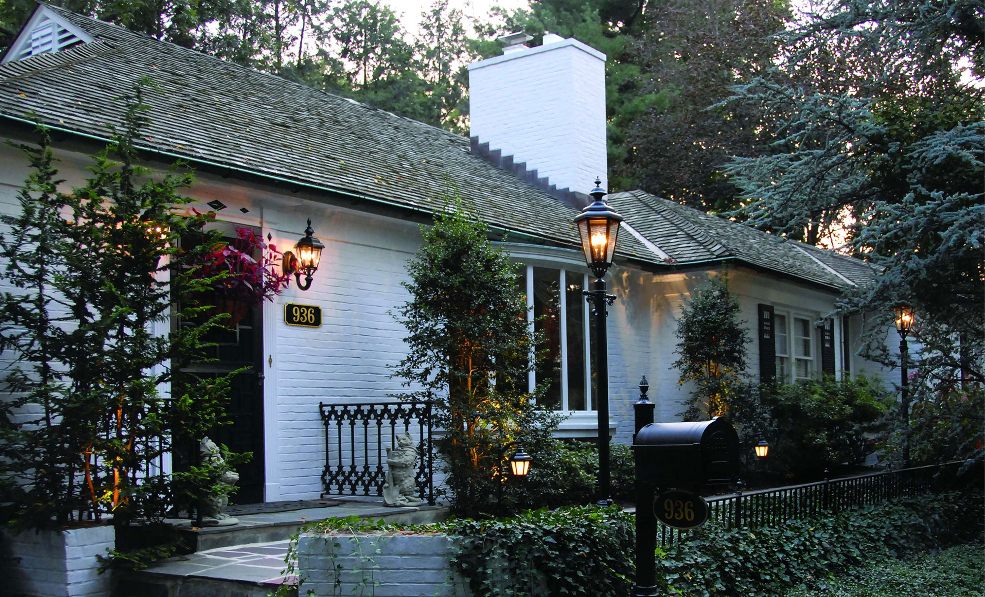 White house with outdoor lighting, a mailbox and shrubs.