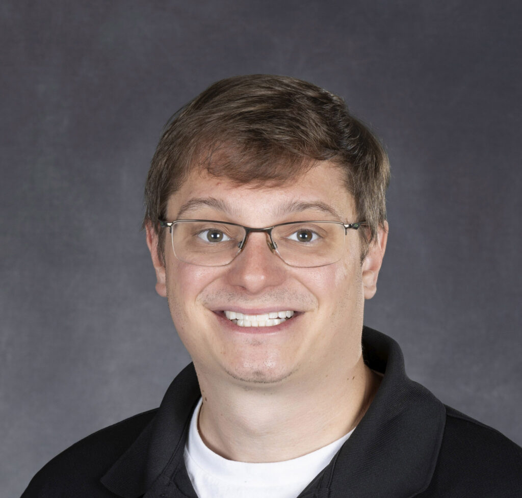 A portrait image of a man smiling and wearing glasses.