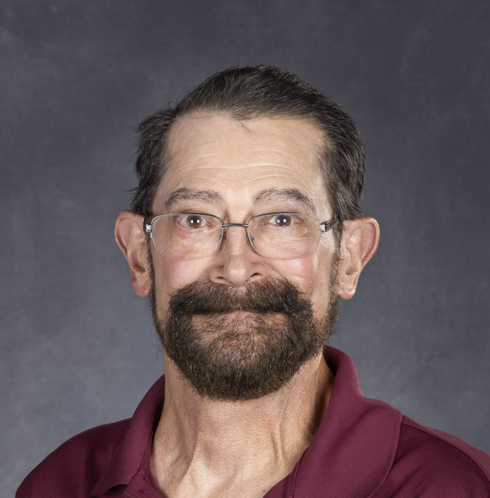 A portrait image of a man with dark hair, a beard, and glasses.